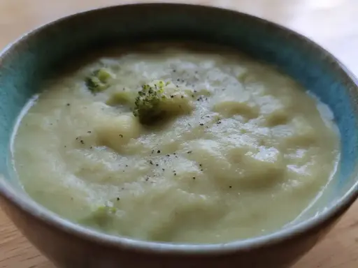 En krämig potatis och broccolisoppa, toppad med lite svartpeppar, serveras i en blå kantad skål.