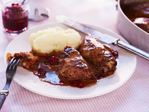 Kåldolmar recept: två kåldolmar med potatismos och lingonsylt, serverade på en tallrik med en gaffel och kniv.