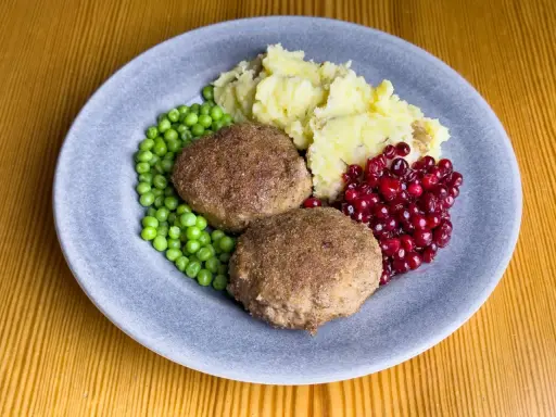 Två köttbullar med potatismos, gröna ärtor och rårörda lingon. En klassisk tallrik med svensk husmanskost.