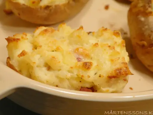 En närbild på en krämig, gratinerad bakad potatis fylld med ost och bacon. En riktig favorit!