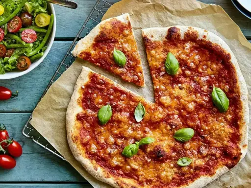 En härlig hemmagjord pizza med tomatsås och ost, toppad med färsk basilika. Bredvid en fräsch sallad med gröna bönor och tomater.
