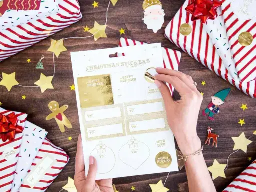 Julklappar inslagna med stjärnor och tomtar. En hand väljer julklappsdekaler, perfekta för julrim barn.
