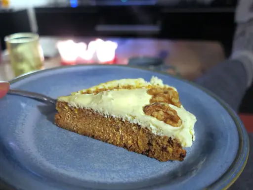 En bit saftig glutenfri morotskaka med krämig frosting och valnötter på en blå tallrik.