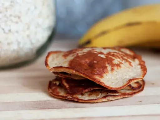 En hög med gyllenbruna, nyttiga pannkakor, gjorda på havregryn och banan, ligger på en träskärbräda.