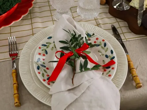 Vacker juldukning dekoration med en tallrik med bär, en vit servett med grönt och rött band, samt bestick med bambuhandtag.