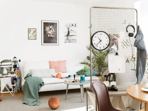 En avslappnad inredning hemma med vit soffa, konst på väggen, en basketboll och en skateboard. En stor klocka hänger på ett metallgaller.