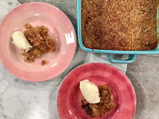 En härlig glutenfri rabarberpaj med en krispig topping, serverad med vaniljglass på rosa och röda tallrikar.