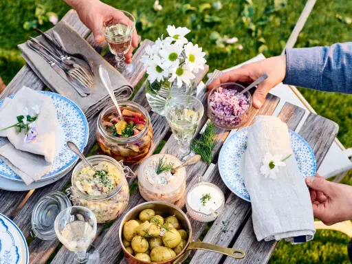 En härlig dukning med vegetarisk midsommarmat: potatissallad, sillinläggningar, gräddfil och hackad rödlök. Blommor och grönska skapar en festlig stämning.