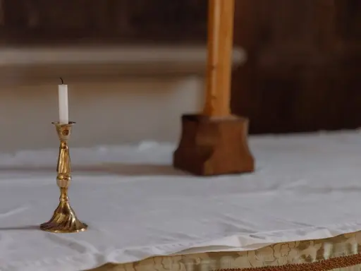 En ljusstake med ett vitt ljus står på ett vitt dukat bord. En träkorsfot skymtar i bakgrunden. Perfekt dop inspiration.