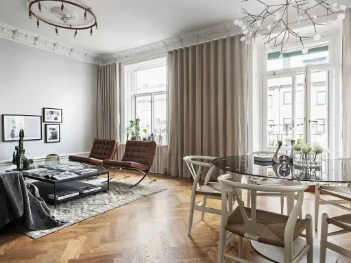 Vardagsrum med många fönster, draperade i ljusa gardiner. Två bruna läderfåtöljer och ett soffbord med böcker.