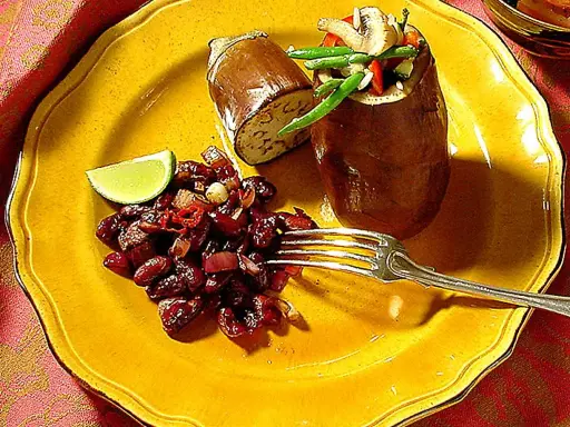 En hel aubergine i ugn, fylld med grönsaker, serveras med en röra av bönor och chili på en gul tallrik.