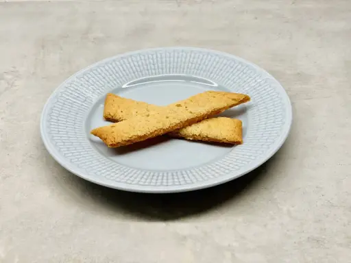 Två gyllene kolasnittar ligger korslagda på en ljusblå tallrik. Perfekt för ett enkelt kolasnittar recept.