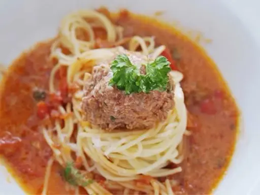 En portion spaghetti med en stor frikadell i en krämig tomatsås, toppad med färsk persilja.