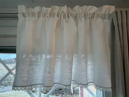 En ljus gardinkappa modern i linne med spetskant. Den hänger på en stång och ger ett mjukt ljusinsläpp.