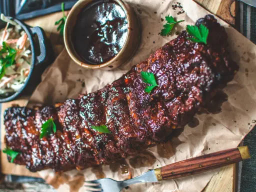 Saftiga spareribs i ugn, glaserade och serverade med en skål coleslaw och BBQ-sås. Perfekt för en härlig middag.