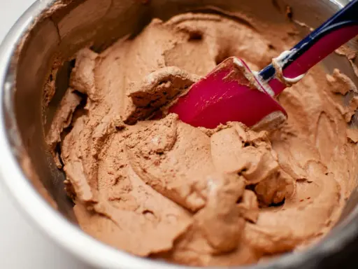 Chokladkräm i en skål, redo att bli glass. En rosa slickepott blandar i den lena smeten, kanske med lite xantangummi för perfekt konsistens.