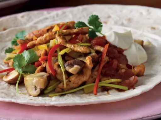 En portion fajitas med kyckling, paprika, champinjoner och lök på en tortilla, serverad med gräddfil. Ett gott fajitas recept!