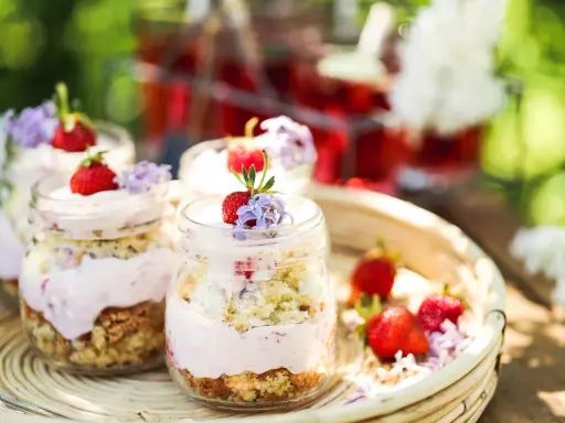 En härlig sommardessert i glasburkar, en himmelsk jordgubbstårta med fluffig grädde och saftiga jordgubbar, dekorerad med små lila blommor.