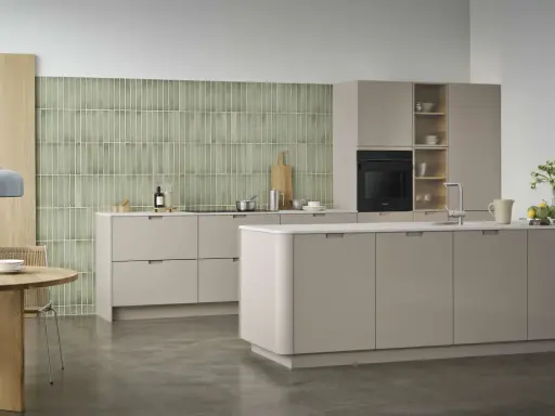 Ett modernt, hållbart kök med beige skåp, grön mosaik och ett runt matbord i trä.