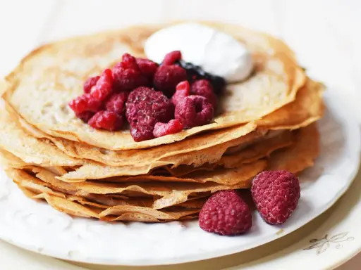 En hög med glutenfria pannkakor toppas med färska hallon och en klick grädde. Perfekt för en frukost eller fika.