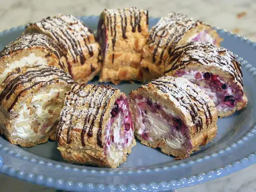 Budapestrulle recept: Skivade rulltårtor med grädde, bär och mandel, toppade med florsocker och chokladdrizzle.