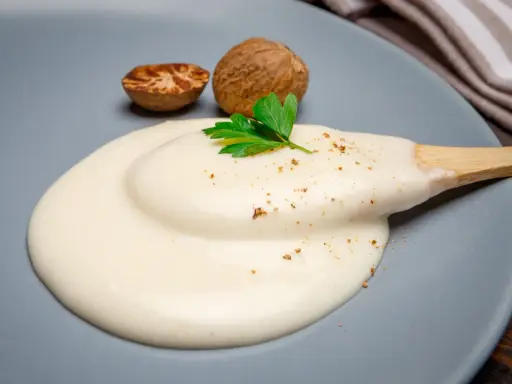 Krämig bechamelsås på en tallrik med muskotnötter och persilja. Ett enkelt bechamelsås recept för alla.