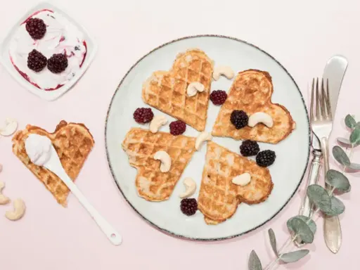 Hjärtformade protein våfflor med bär och cashewnötter. En skål med yoghurt och bär står bredvid.