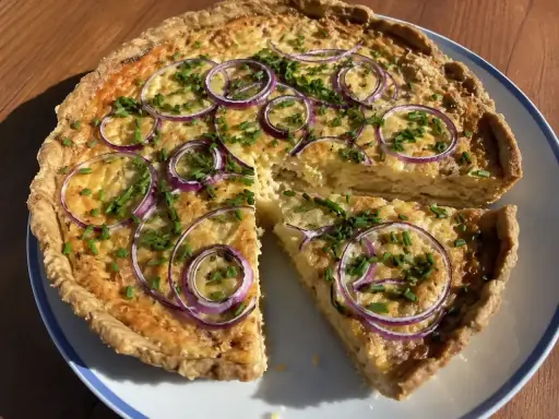 En gyllene ostpaj med rödlök och gräslök, perfekt för ett ostpaj recept. En bit är uppskuren.
