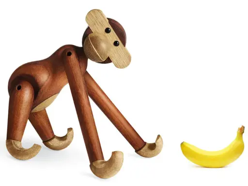 En träapa från Kay Bojesen tittar nyfiket på en banan. Olika kay bojesen apa storlekar finns tillgängliga.