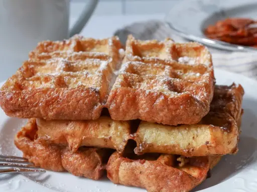 En stapel gyllene franska våfflor, pudrade med florsocker, väntar på att avnjutas. En härlig frukost eller fika.