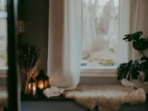 Mysig fönsterbräda med fårskinn, ljuslyktor och tunna gardiner som släpper in ett mjukt ljus.