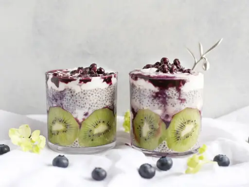Två glas med chia pudding recept, fyllda med kiwi, yoghurt och blåbär. En vacker och hälsosam frukost.