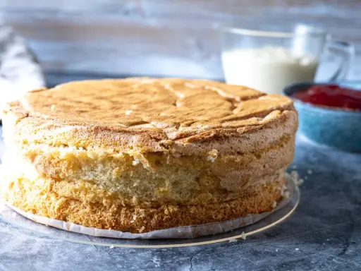 En fluffig tårtbotten, redo för fyllning. Perfekt för ditt tårtbotten recept. Bredvid syns grädde och sylt.
