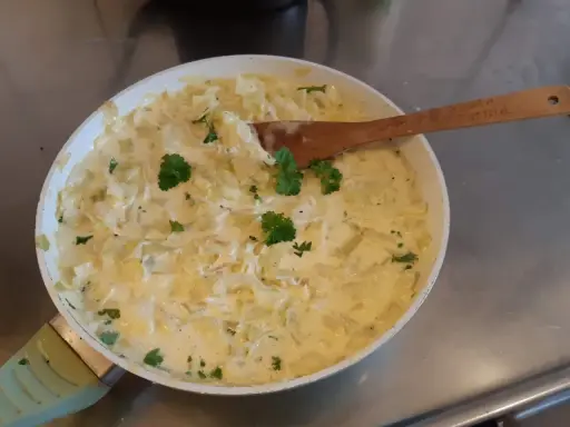 Krämig stuvad vitkål i en panna, garnerad med persilja. En klassisk svensk rätt som doftar hemtrevnad.