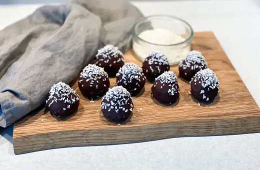 Mörka, chokladöverdragna protein chokladbollar toppade med kokosflingor ligger på en träskärbräda.