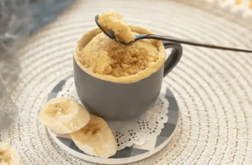 En fluffig mugcake proteinpulver med bananskivor. En sked lyfter en bit av den läckra kakan.