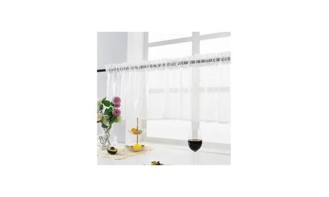 Vit gardinkappa och längder med spetskant hänger för ett fönster. Blommor, frukt och ett glas vin på fönsterbrädan.