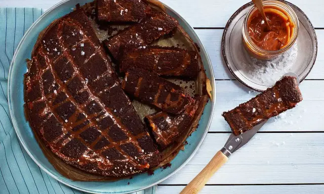 Chokladkaka med kolasås och havssalt, perfekt att baka glutenfritt. En bit lyfts upp med en kniv.