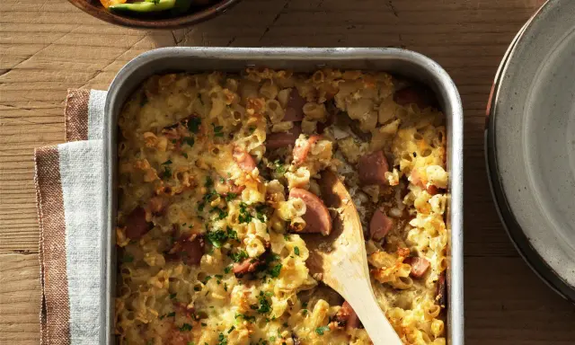 En gyllene makaronilåda med korv, toppad med persilja, redo att serveras. En klassisk svensk rätt som värmer själen.