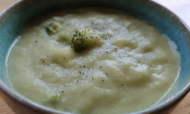 En krämig potatis och broccolisoppa, toppad med lite svartpeppar, serveras i en blå kantad skål.