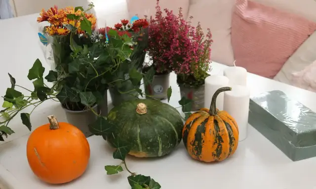 Förberedelser för att dekorera pumpa med höstblommor, ljus och murgröna.