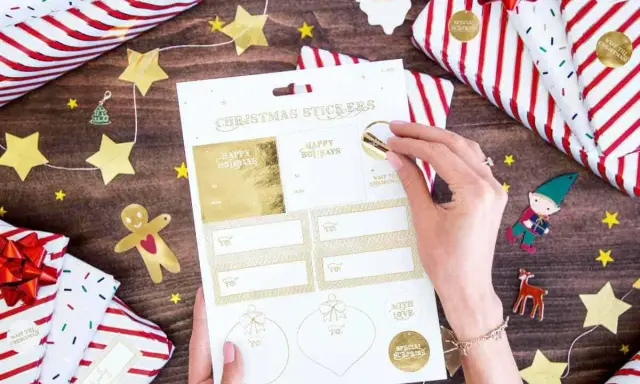 Julklappar inslagna med stjärnor och tomtar. En hand väljer julklappsdekaler, perfekta för julrim barn.