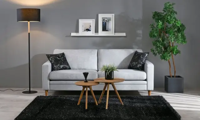 Grå soffa med svarta kuddar, två runda träbord, svart matta och golvlampa. Bra inredningstips för ett modernt vardagsrum.