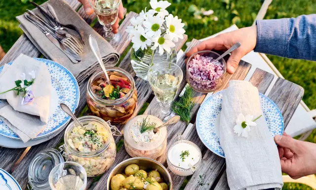 En härlig dukning med vegetarisk midsommarmat: potatissallad, sillinläggningar, gräddfil och hackad rödlök. Blommor och grönska skapar en festlig stämning.