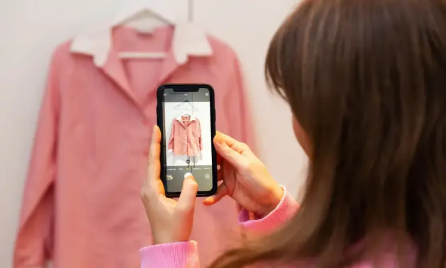 En person fotograferar en rosa skjorta med sin mobiltelefon. Ett bra exempel på varför man ska köpa second hand – unika fynd!
