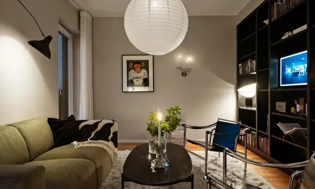 Mysig vardagsrumsmiljö med en stor papperslampa i taket. Belysning bakom gardin skapar en mjuk atmosfär.