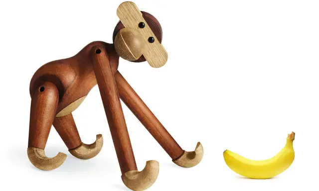 En träapa från Kay Bojesen tittar nyfiket på en banan. Olika kay bojesen apa storlekar finns tillgängliga.