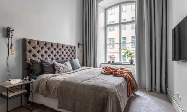 Sovrum med en stor säng, en taklampa och en **gardin på ena sidan av fönstret**.