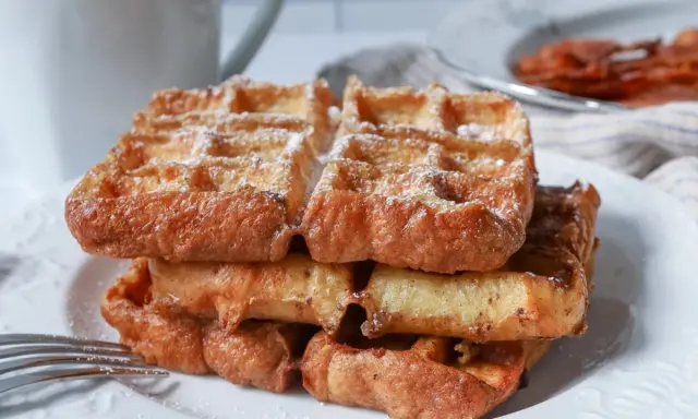 En stapel gyllene franska våfflor, pudrade med florsocker, väntar på att avnjutas. En härlig frukost eller fika.