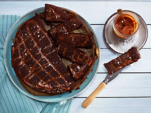 Chokladkaka med kolasås och havssalt, perfekt att baka glutenfritt. En bit lyfts upp med en kniv.